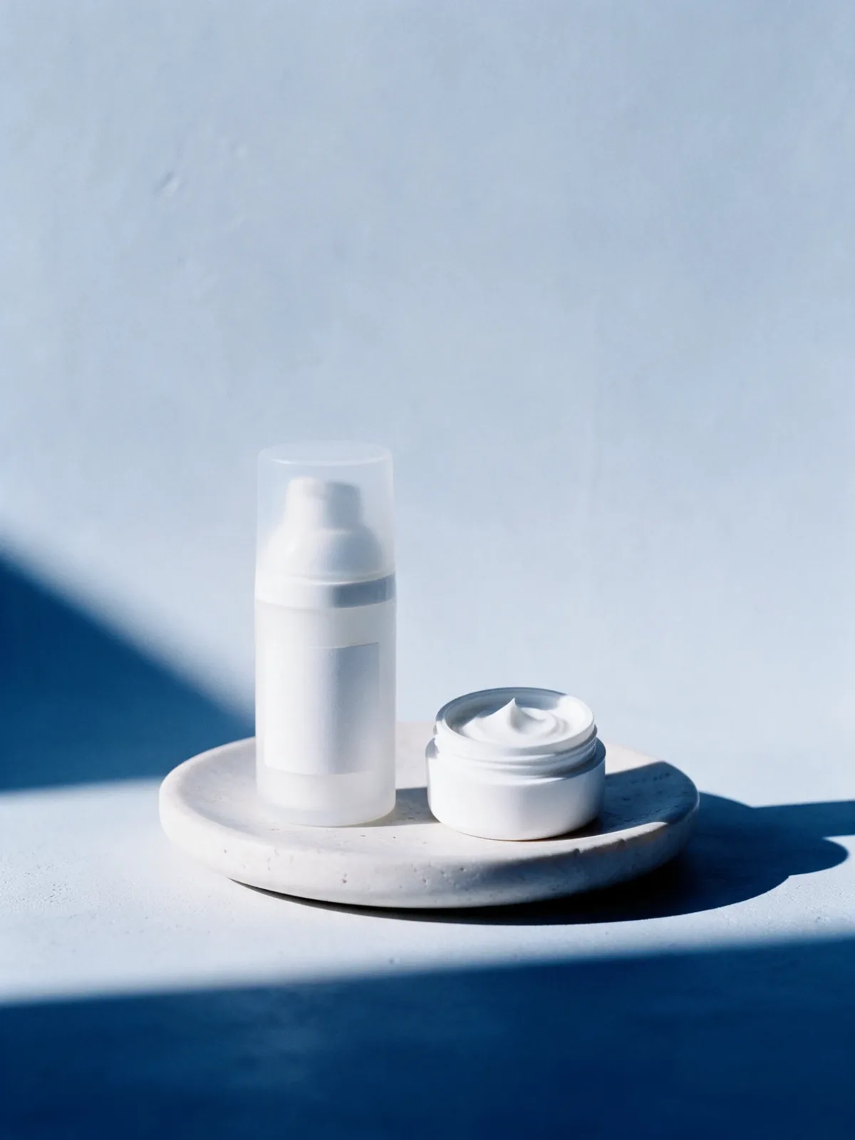 Frasco pump fosco e pote aberto de creme branco sobre pedestal de pedra